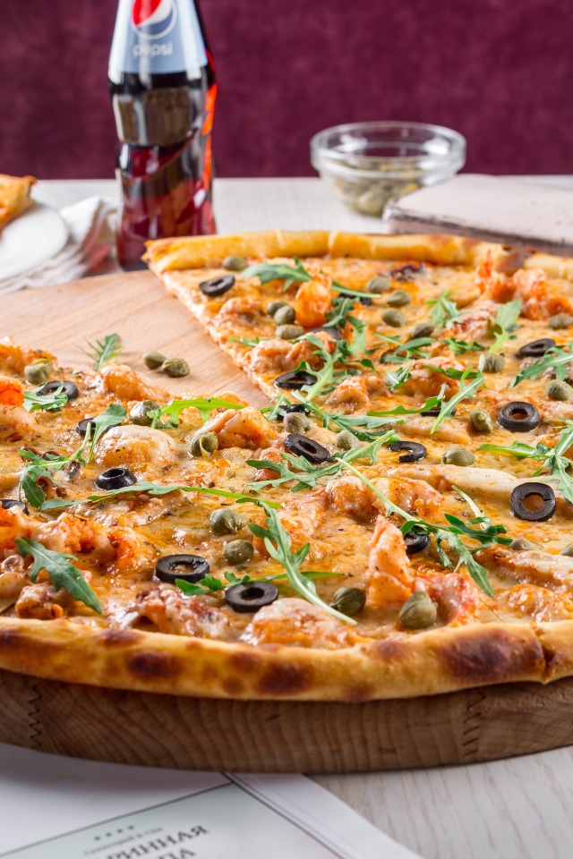 Большая аппетитная пицца с маслинами на столе в кафе