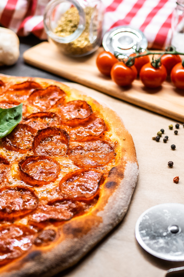 Пицца пепперони на столе с овощами и специями