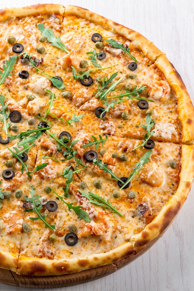 Pizza with seafood, arugula and olives on the table