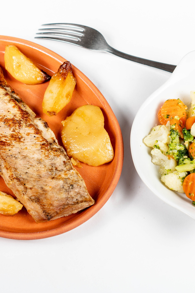 Кусок запеченной рыбы на тарелке с овощами 