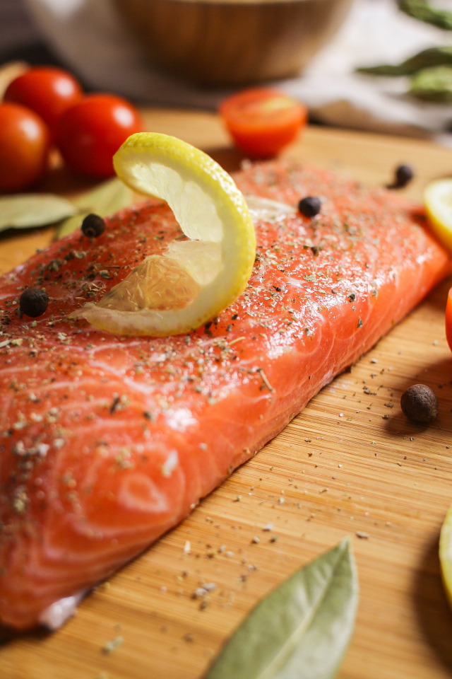 Кусок красной рыбы на доске с лимоном и помидорами