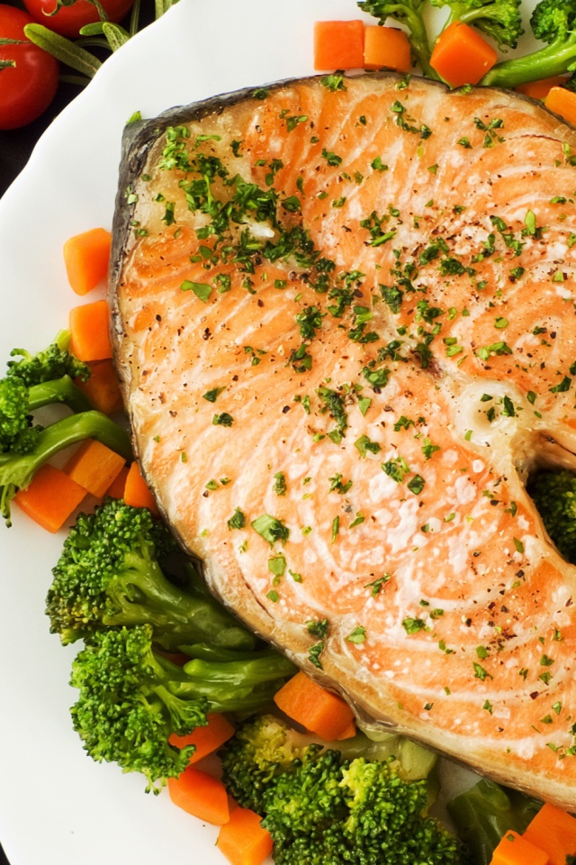 Кусок красной рыбы на тарелке с морковью и брокколи 