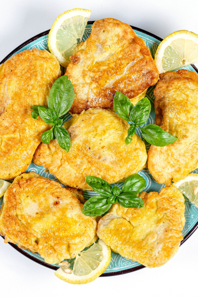 Appetizing fish in batter on a plate with lemon slices and cutlery