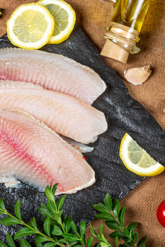 Филе рыбы на столе с лимоном, помидорами и оливками