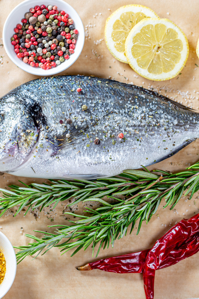 Fresh fish on the table with spices, lemon, rosemary and red pepper