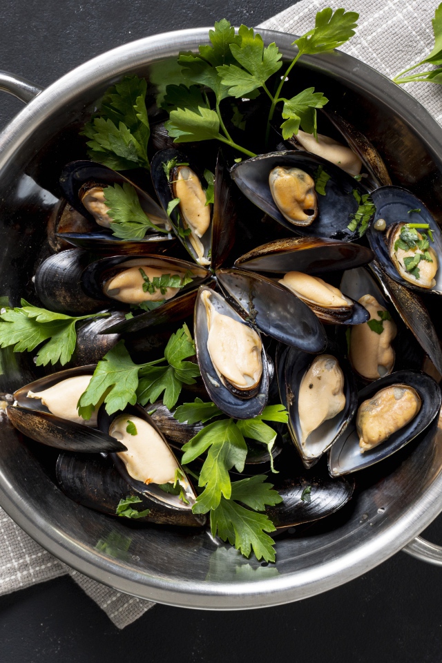 Свежие мидии в кастрюле с зеленью петрушки 