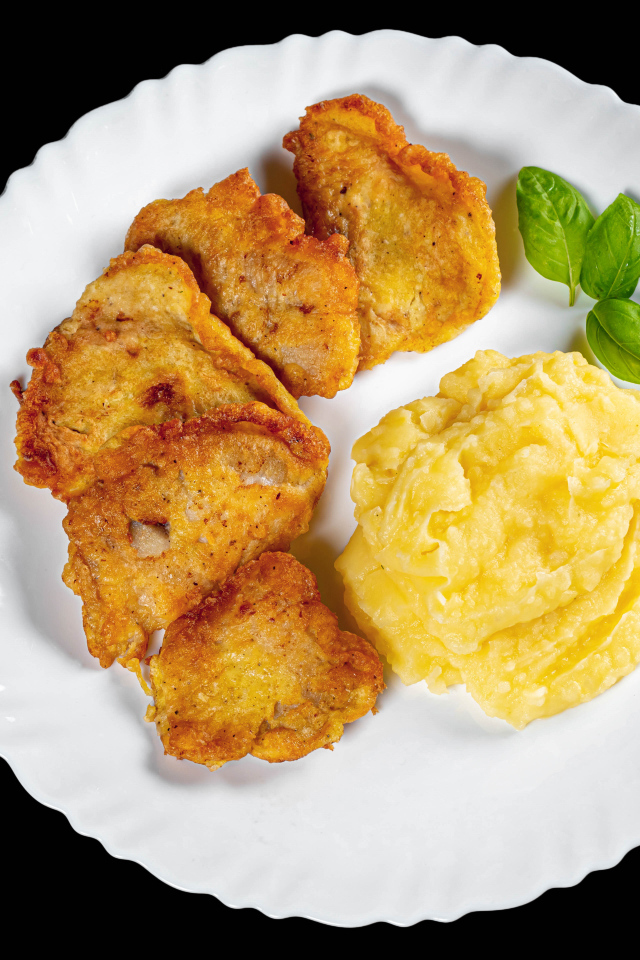 Куски жареной рыбы с картофельным пюре в тарелке на черном фоне