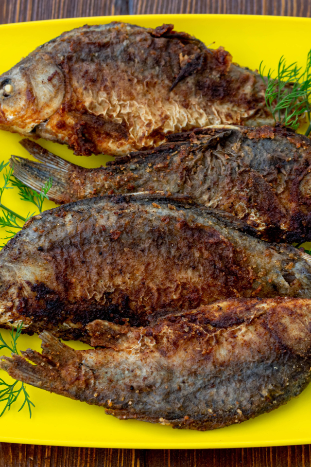 Жареные караси с укропом на желтой тарелке 