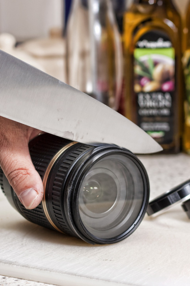 Мужчина нарезает ножом объектив фотоаппарата 