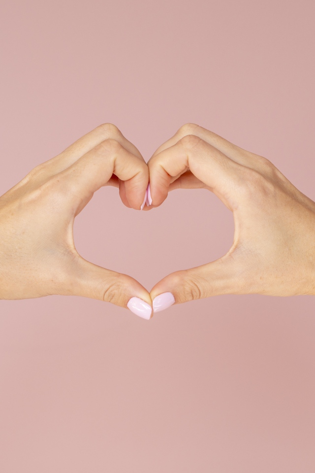 Девушка делает сердце руками на розовом фоне 