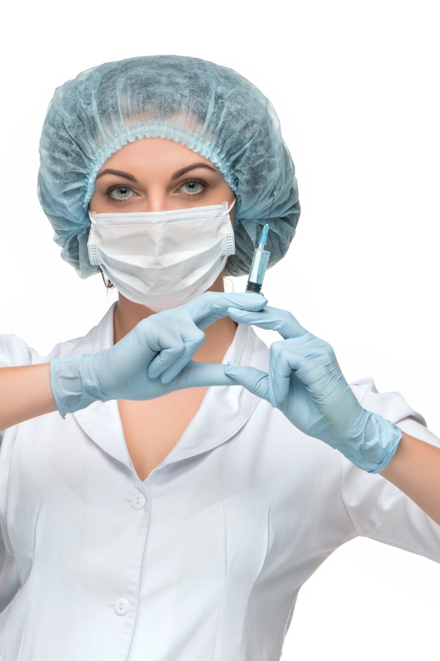 Девушка медсестра в маске со шприцем в руках на белом фоне