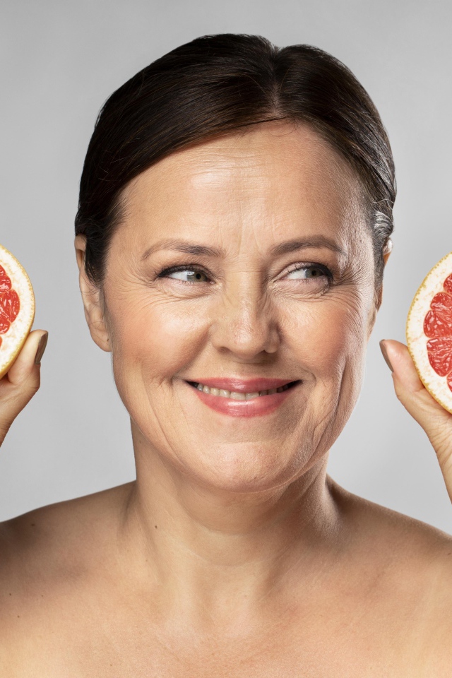 Улыбающаяся женщина с грепфрутом в руках на сером фоне
