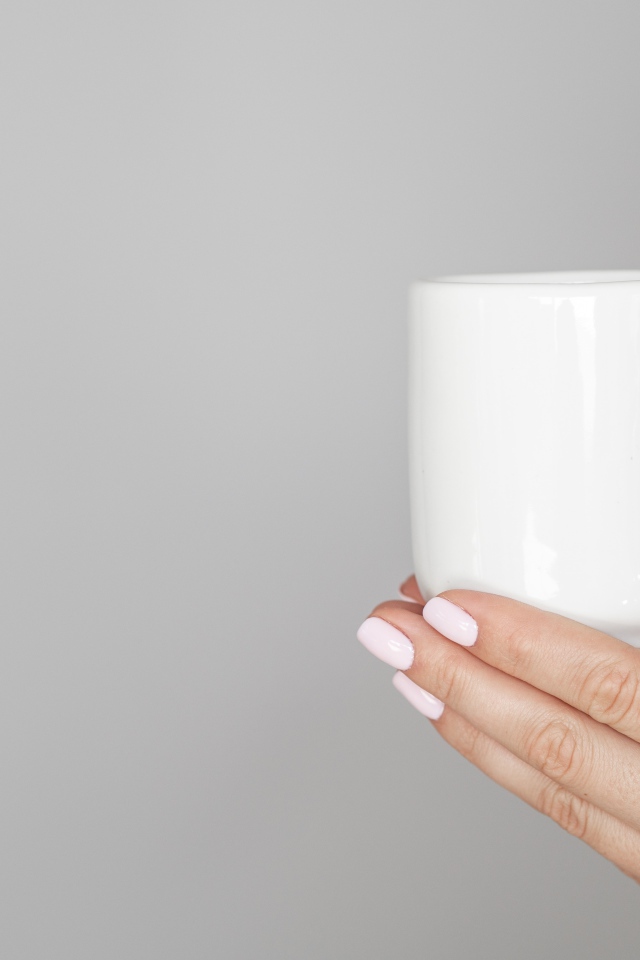 Белая кружка в руках девушки на сером фоне