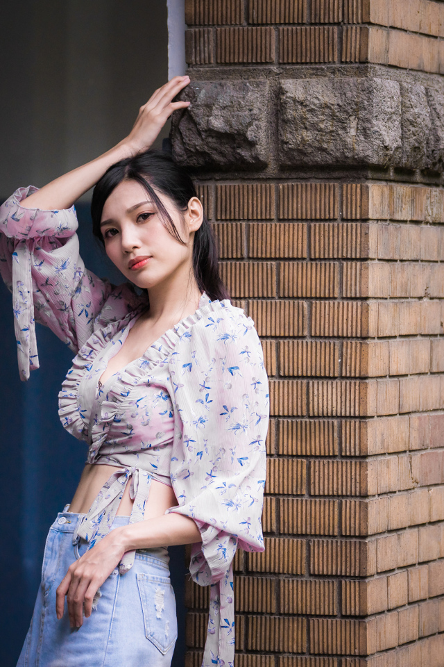 Красивая девушка азиатка стоит у кирпичной колонны 