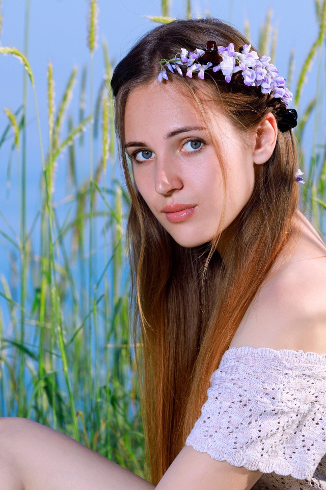 Красивая молодая девушка с венком на голове сидит на поле с колосьями 