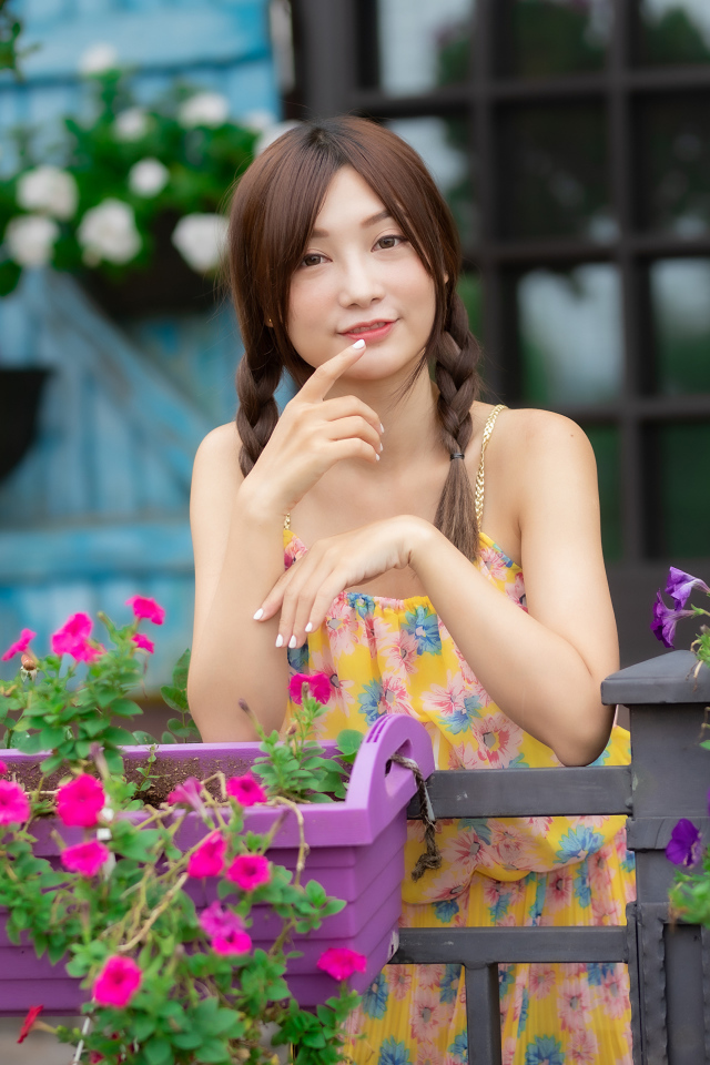 Милая азиатка стоит у кашпо с цветами петунии 