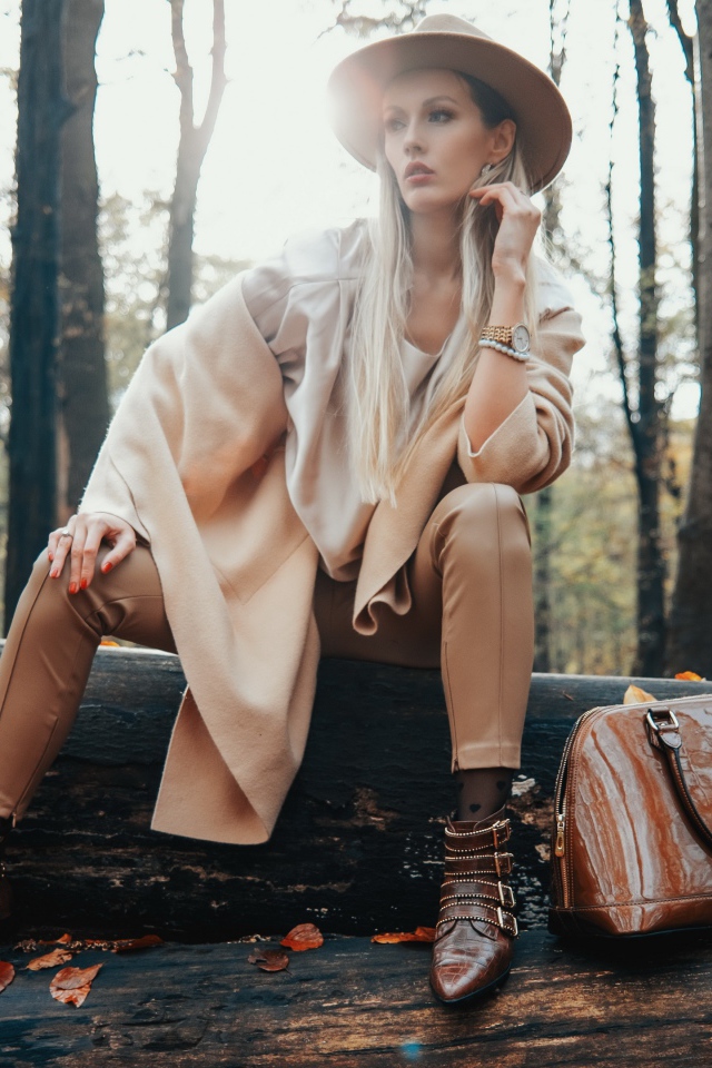 Девушка в пальто сидит на упавшем дереве в лесу 