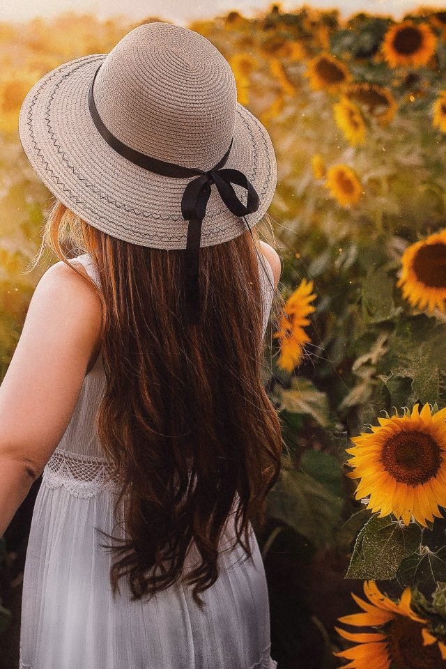 Девушка в белом платье и шляпе гуляет по полю с подсолнухами