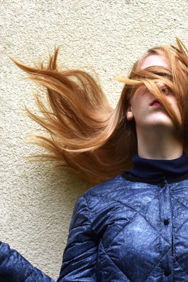 Девушка с волосами на лице стоит у стены