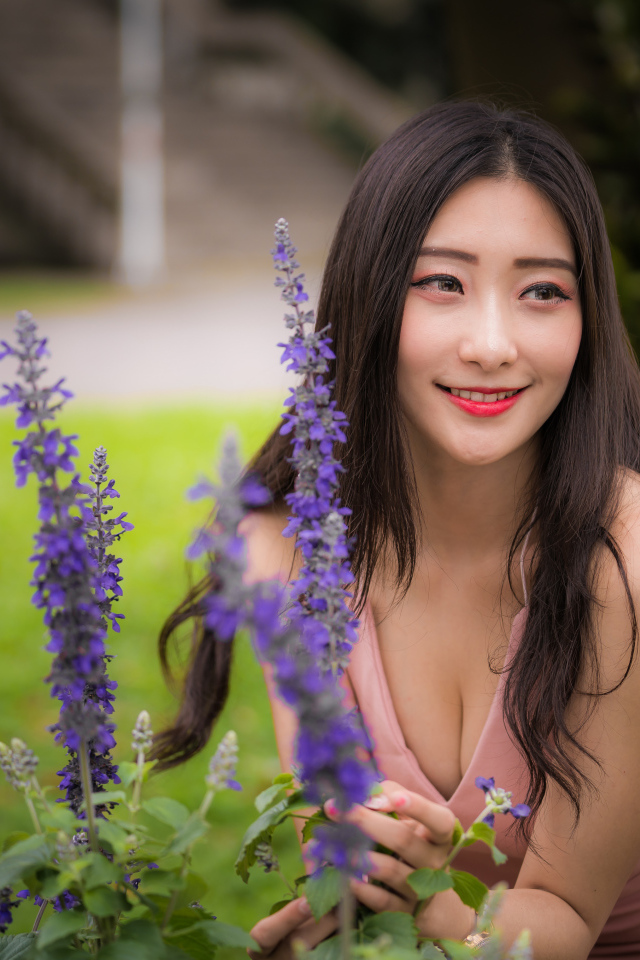 Улыбающаяся азиатка стоит у синих цветов 