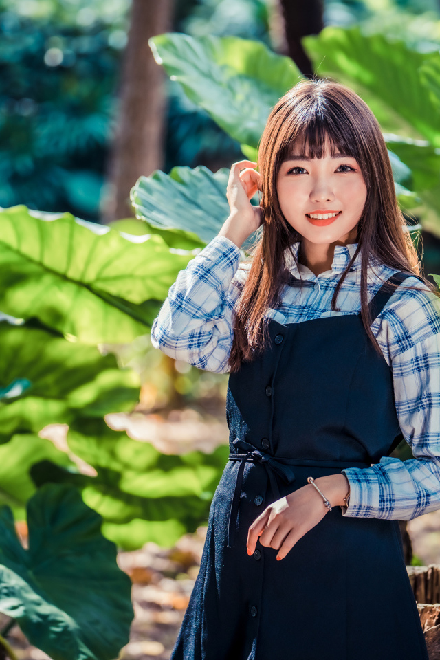 Улыбающаяся девушка азиатка в черном платье стоит в парке