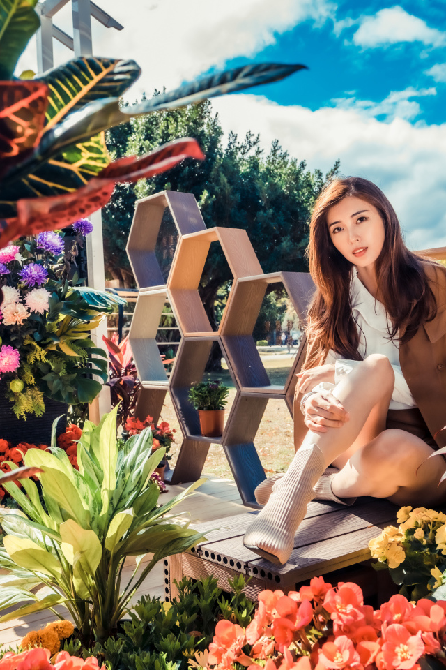 Молодая азиатка сидит возле клумбы с цветами