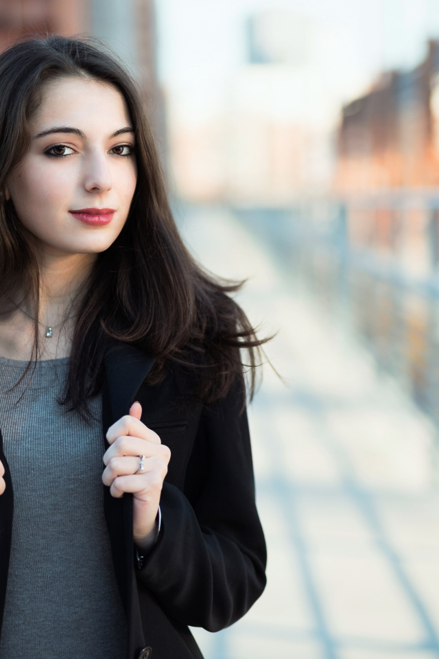 Молодая девушка в черном пальто стоит на мосту