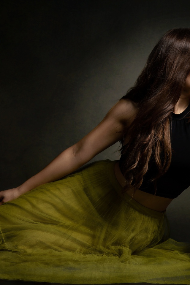 Молодая девушка в длинной юбке сидит на полу