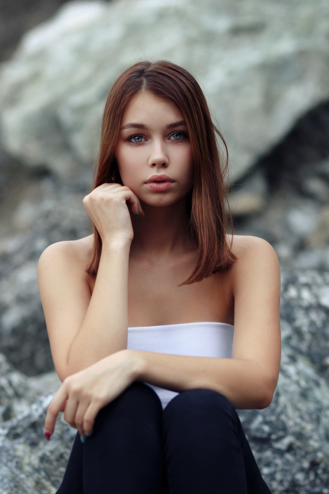 Молодая девушка сидит на камнях 