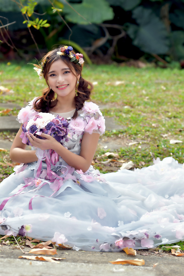 Девушка азиатка в красивом платье сидит на земле с букетом 