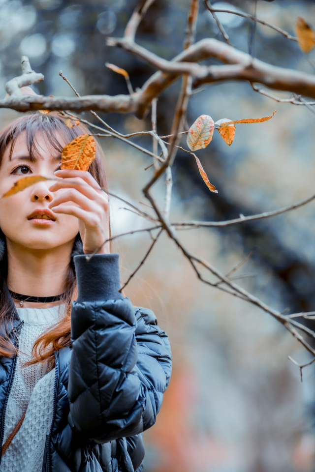 Девушка азиатка в черной куртке у дерева