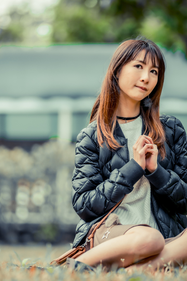 Девушка азиатка в черной куртке сидит под деревом