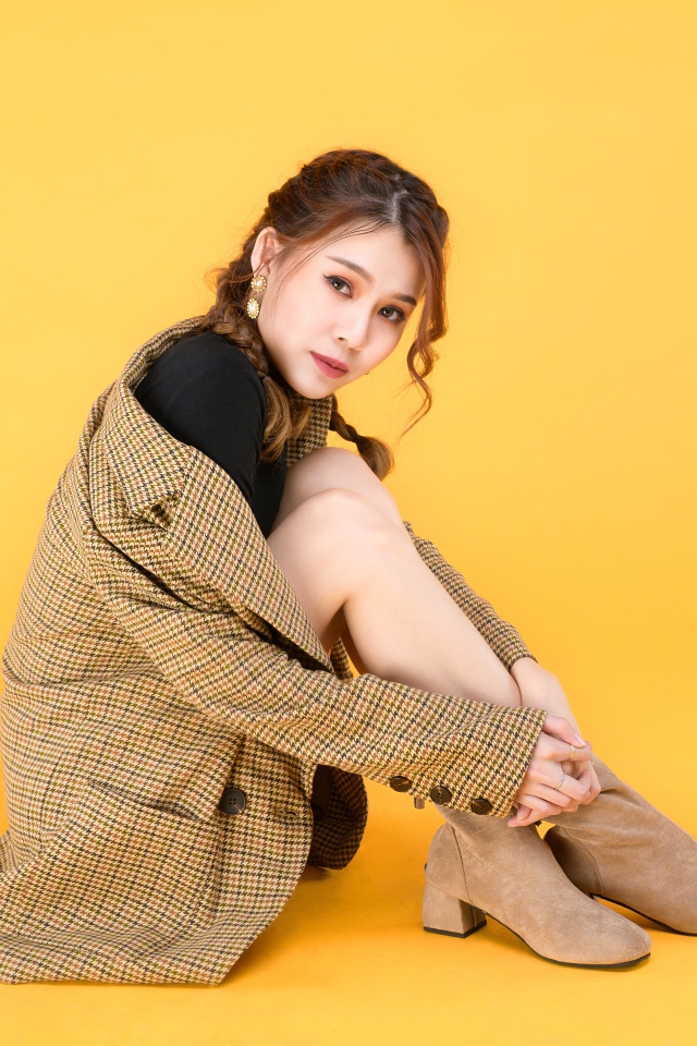 Девушка азиатка в пальто на желтом фоне 