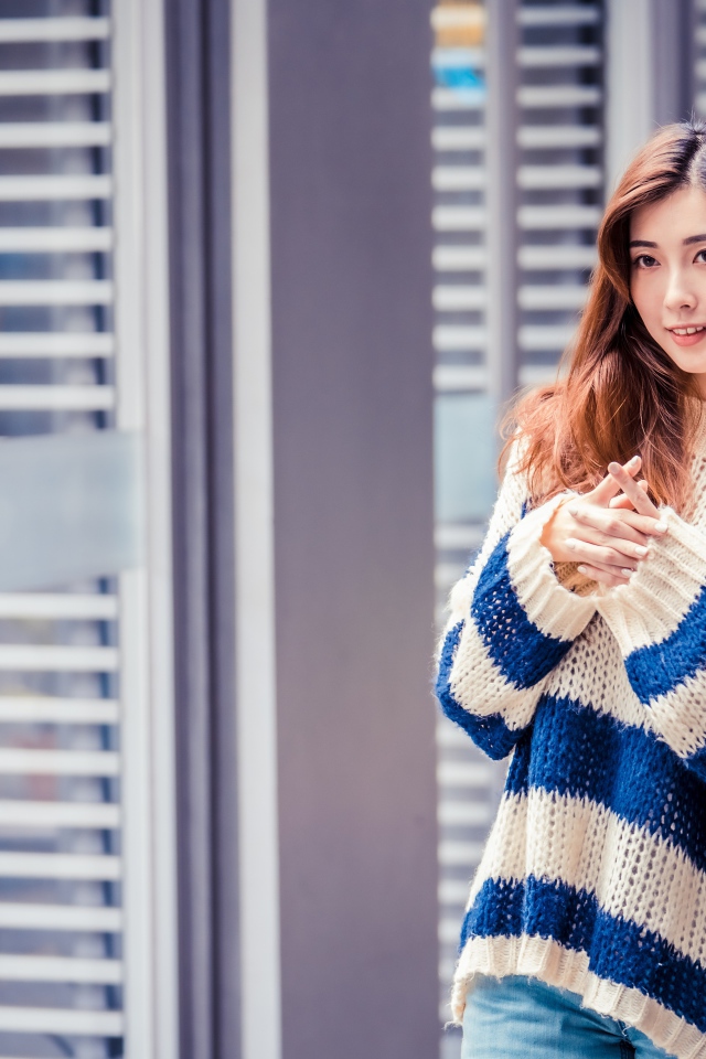 Девушка азиатка в теплом свитере стоит у окна