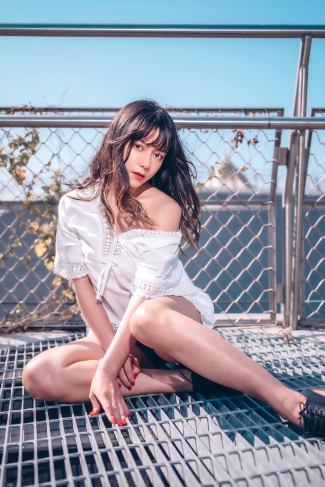 Девушка азиатка в белом наряде сидит на сетке