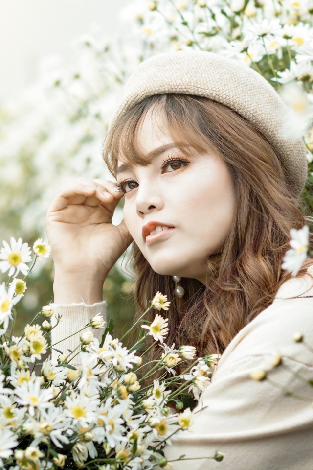 Девушка азиатка сидит в белых цветах ромашки 