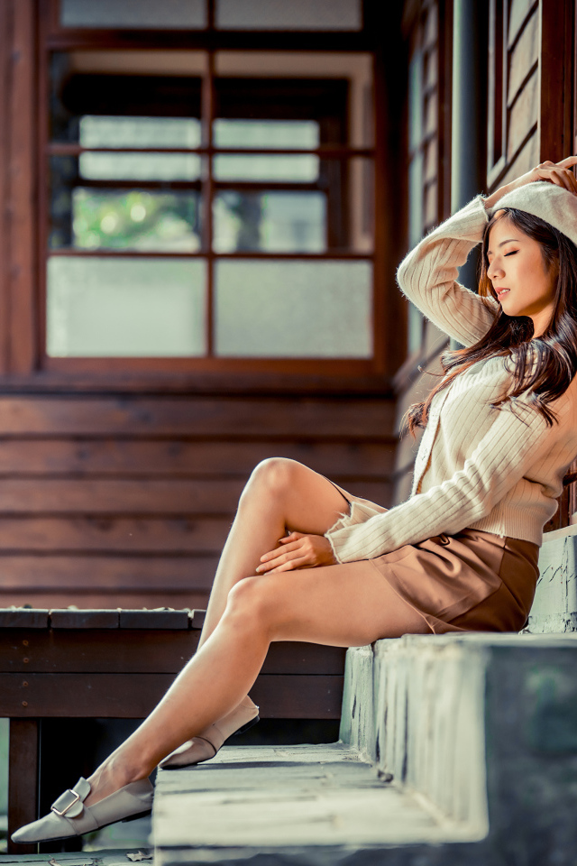 Девушка азиатка с закрытыми глазами сидит на ступеньках дома 