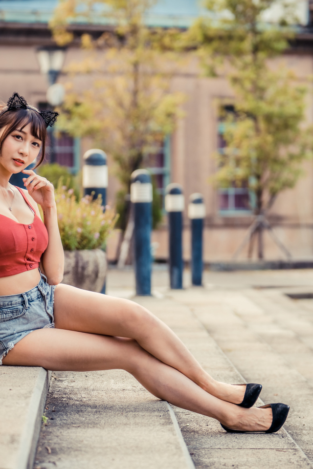 Азиатка в шортах сидит на ступенях 