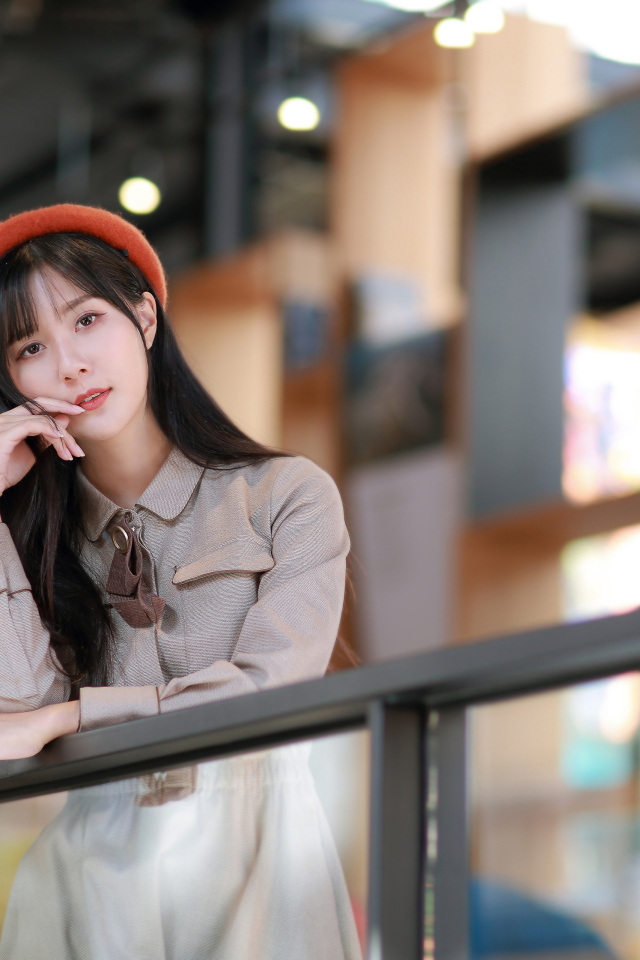 Азиатка в сером платье стоит у перил 