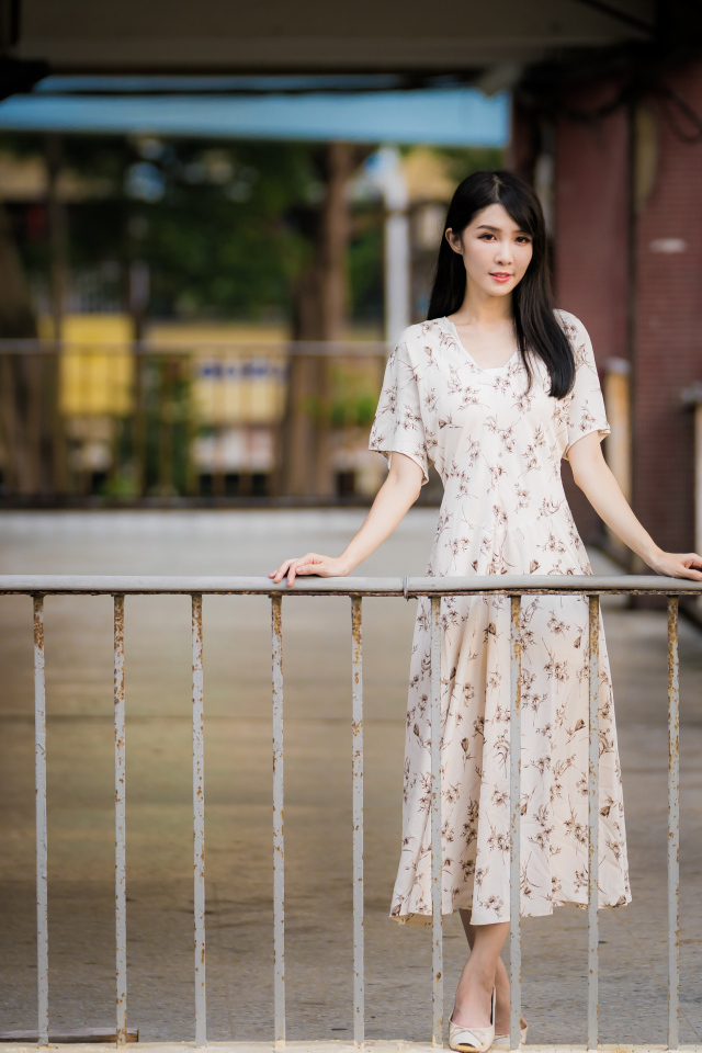 Красивая азиатка в платье стоит у перил