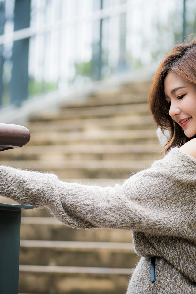 Красивая девушка азиатка в сером свитере на ступеньках 