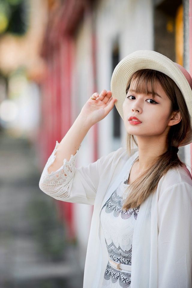 Красивая азиатка в шляпе стоит у стены