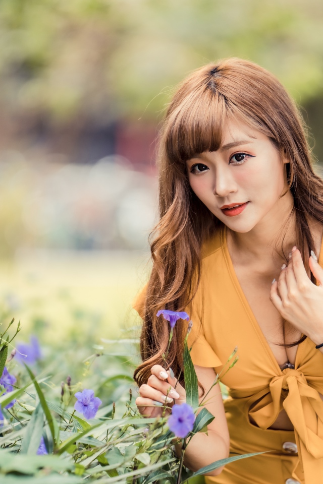 Красивая девушка азиатка в желтом платье у фиолетовых цветов 