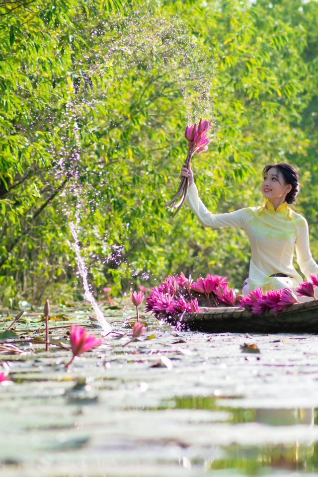 Красивая девушка азиатка на лодке рвет цветы лотоса в реке