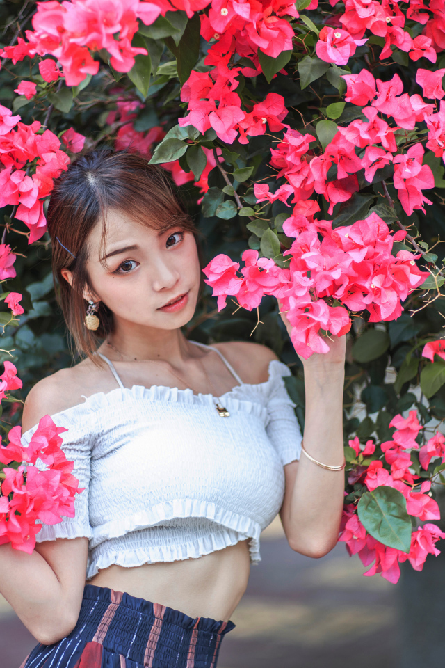 Красивая азиатка стоит у дерева с красными цветами