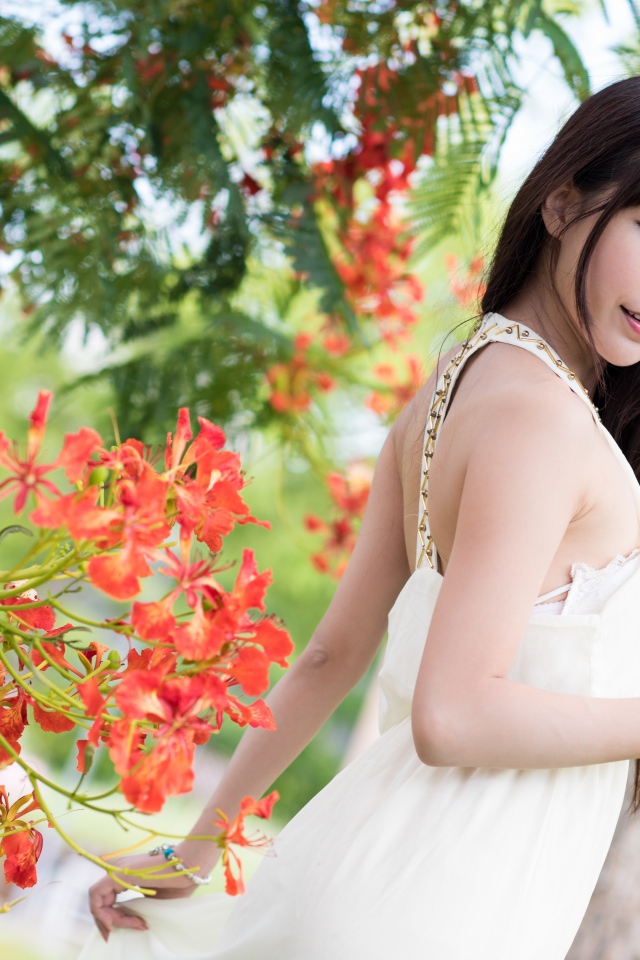 Красивая девушка азиатка в красном платье у дерева с цветами