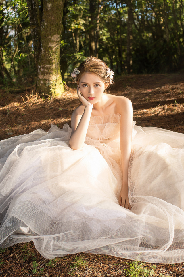 Красивая девушка азиатка в белом свадебном платье сидит на земле