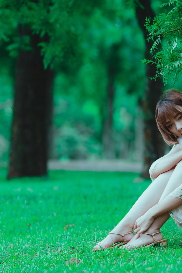 Красивая девушка азиатка сидит на зеленой траве в парке 