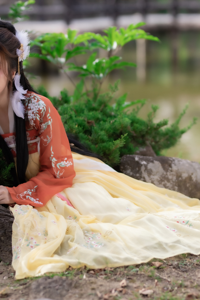 Красивая девушка азиатка сидит на земле у дерева 