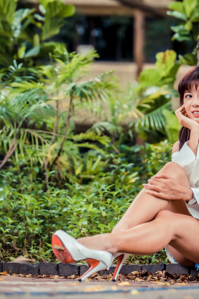 Красивая девушка азиатка сидит на земле в парке 